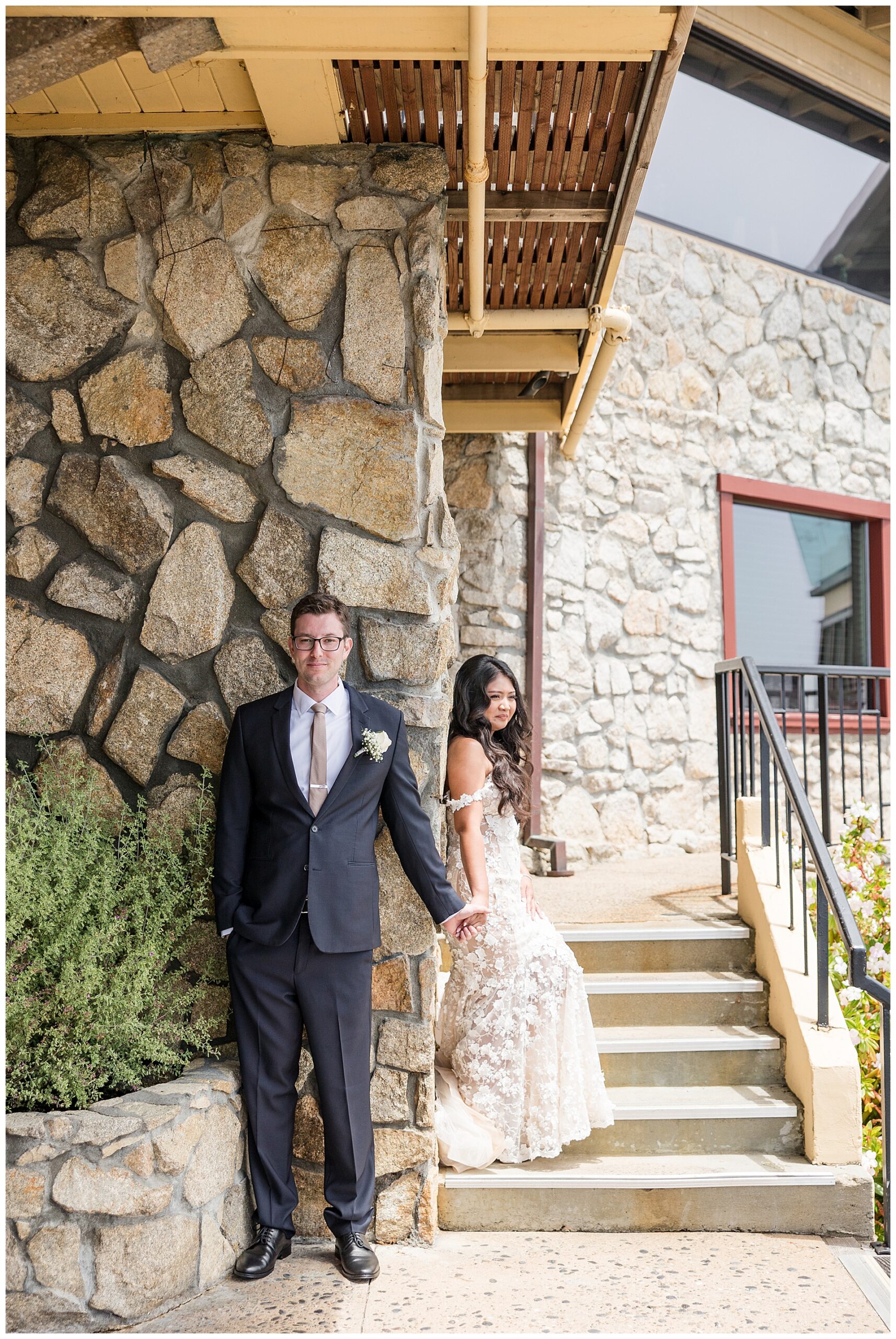 Bride and Groom share a first touch around a rock wall of the Hyatt Carmel Highlands venue. 